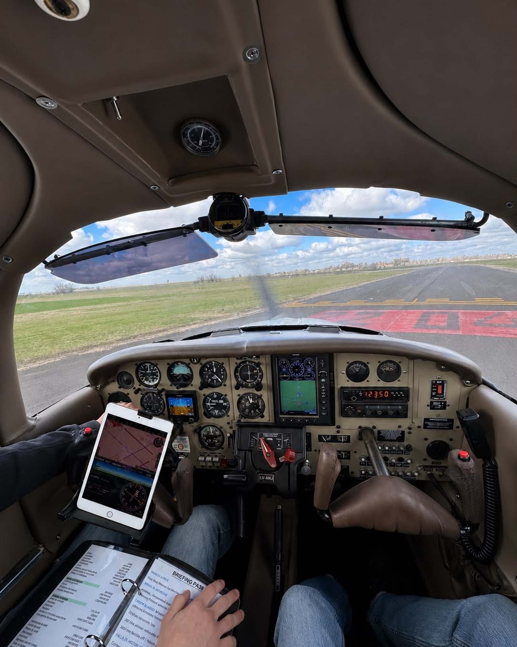 Cabina del Piper PA-38 LV-ANJ desde el asiento del alumno, con el briefing sobre las rodillas y la pista de Venado Tuerto al frente